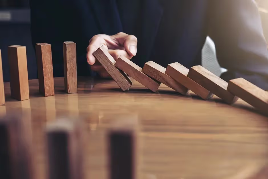 Hand stopping a row of falling wooden dominoes
