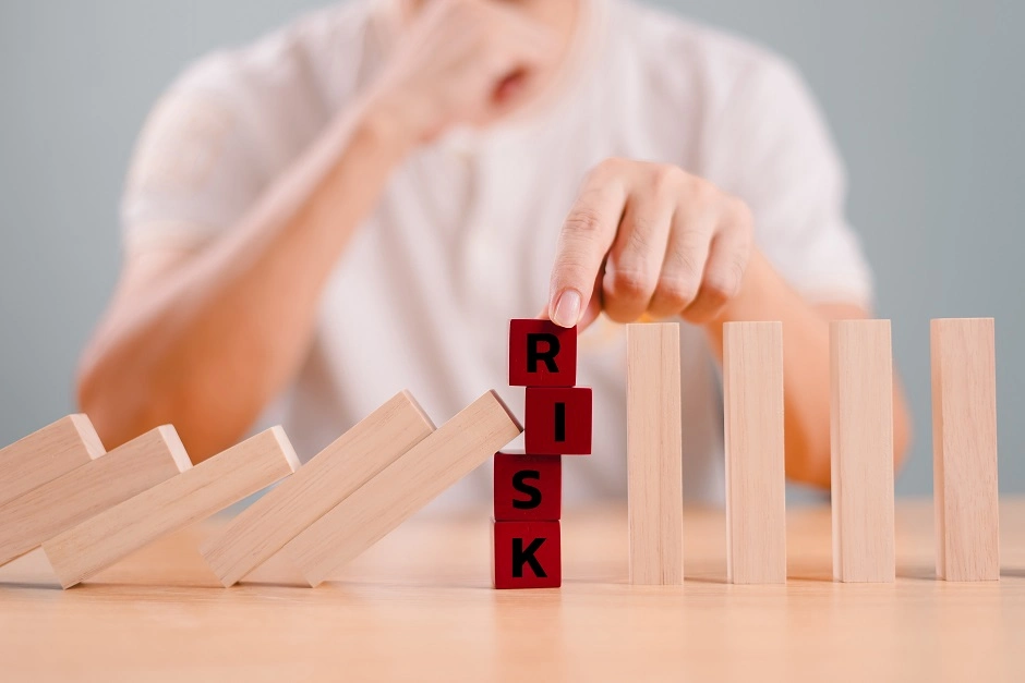 Hand stopping falling wooden dominoes with red blocks spelling RISK