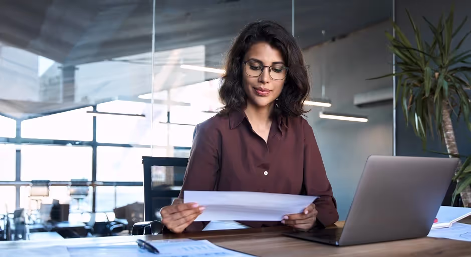 Businesswoman in glasses reading a document at her laptop