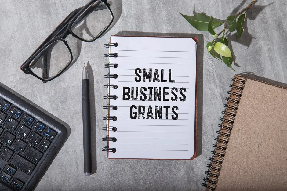 Notebook reading "Small Business Grants" with glasses, pen and keyboard on a desk