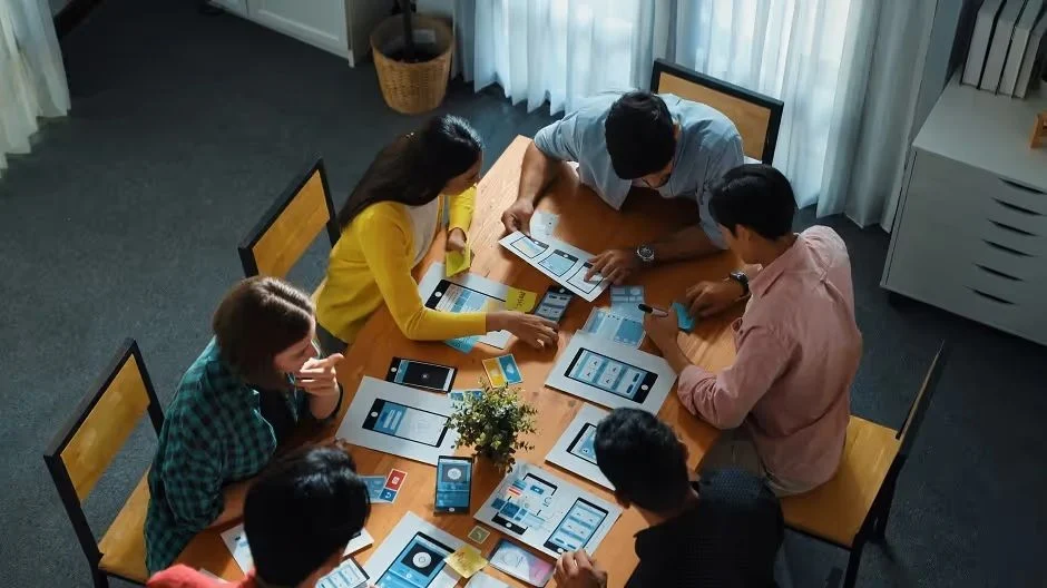 Team around a table with phone and app design sketches, seen from above