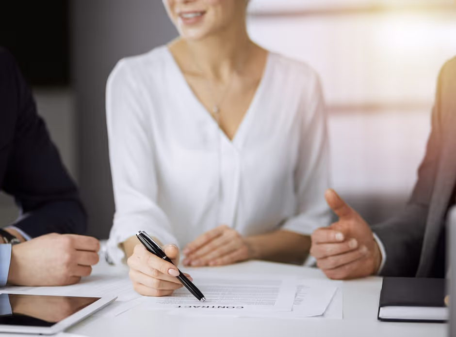 Woman pointing a pen at a contract as two people discuss it across a table