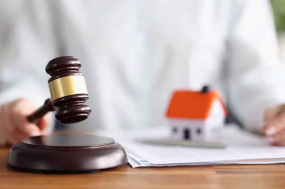 Gavel striking a sound block beside a small model house and papers