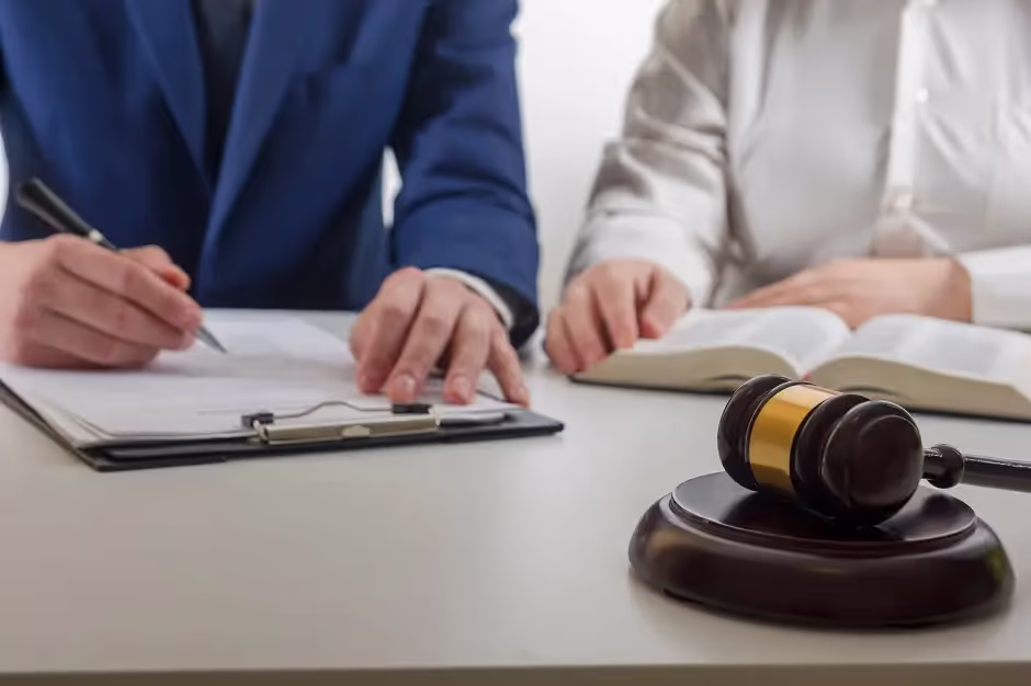 Person signing a document on a clipboard beside a gavel