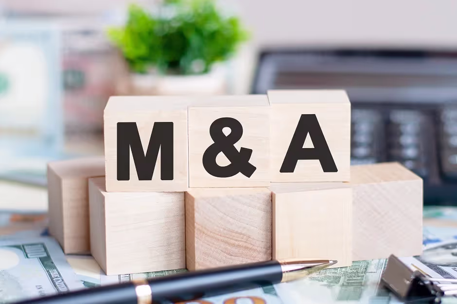 Wooden blocks spelling M&A on a desk with cash and a pen