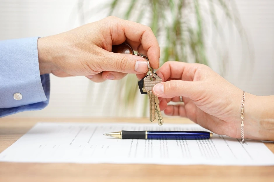 Landlord handing keys to a tenant over a signed lease and a pen