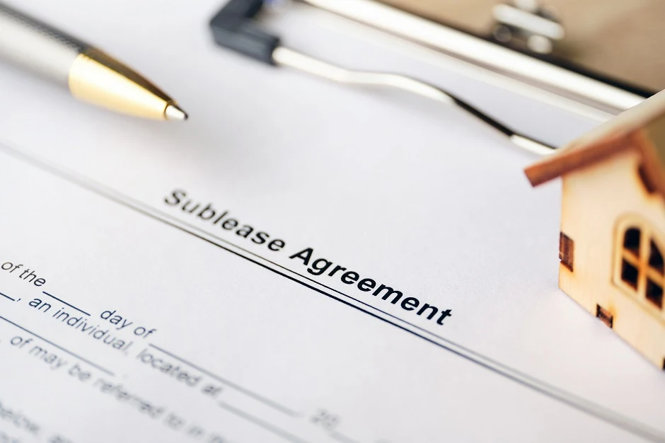 Sublease agreement form with a pen, a clipboard and a small wooden house model