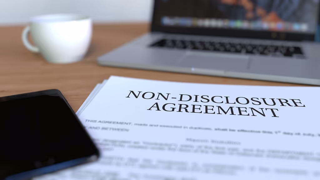 Non-disclosure agreement on a desk beside a laptop, phone and coffee cup