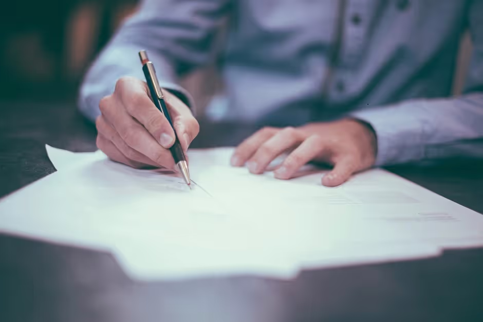 Person signing a document with a pen at a desk