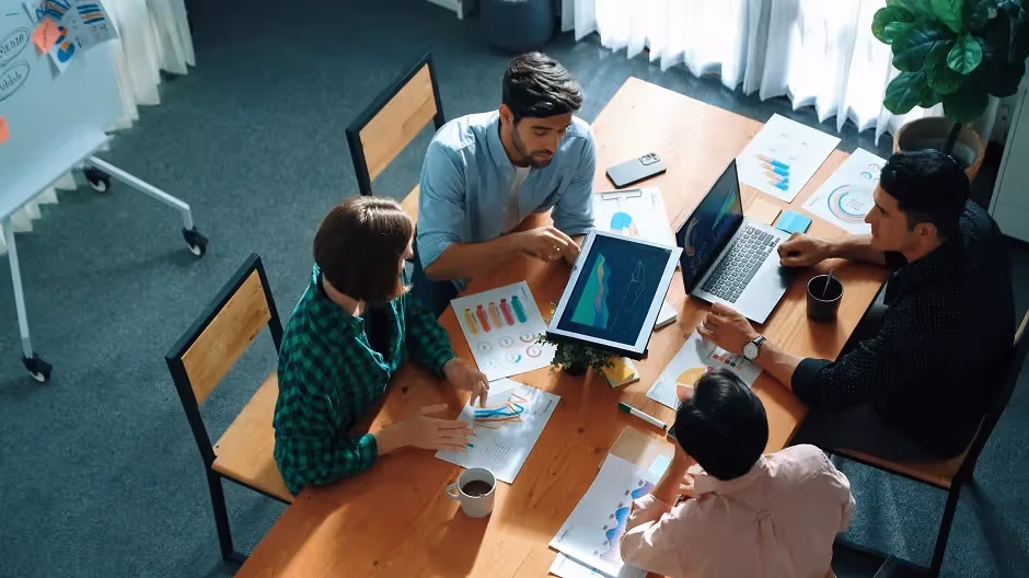 Overhead view of a team working with laptops and charts at a wooden table