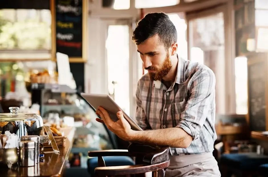 Café owner in a plaid shirt checking a tablet behind the counter