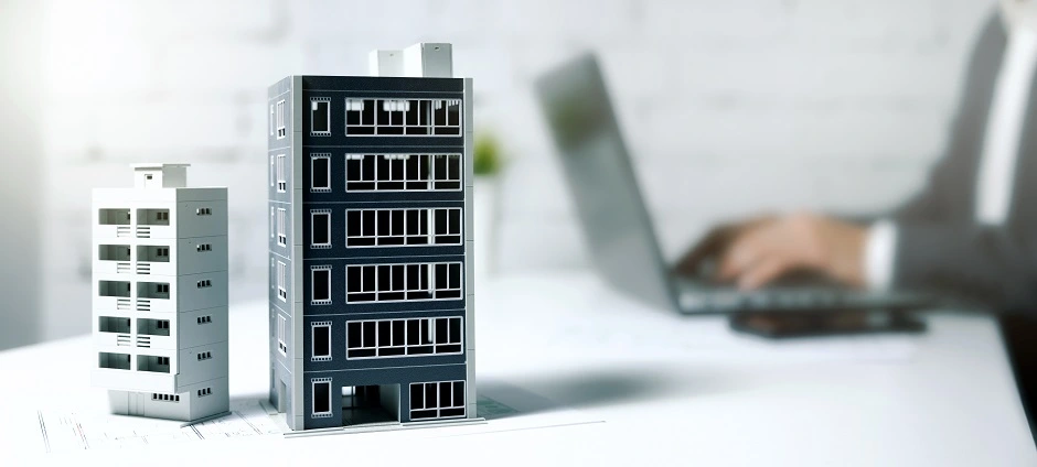 Model office buildings on a desk in front of a person using a laptop