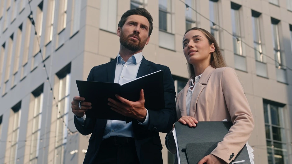 Two business professionals holding folders outside an office building