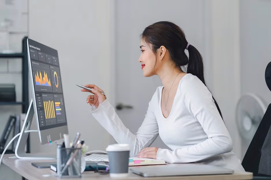 Woman at a desk reviewing performance charts on a computer monitor