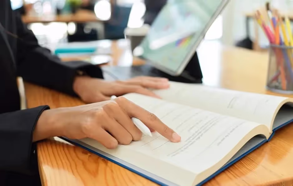 Person following text with a finger in an open book at a desk