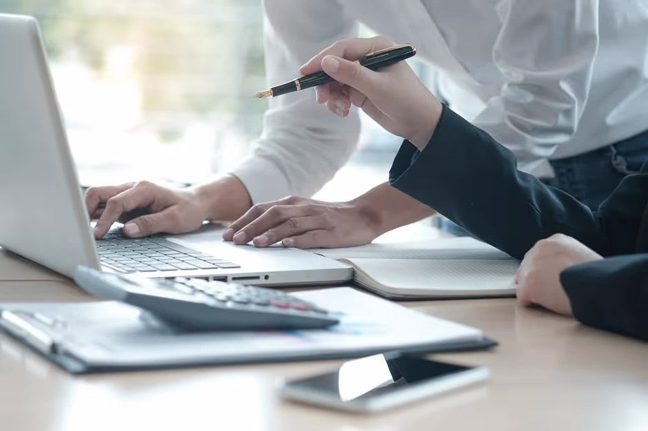 Colleagues working together at a laptop with a calculator and clipboard