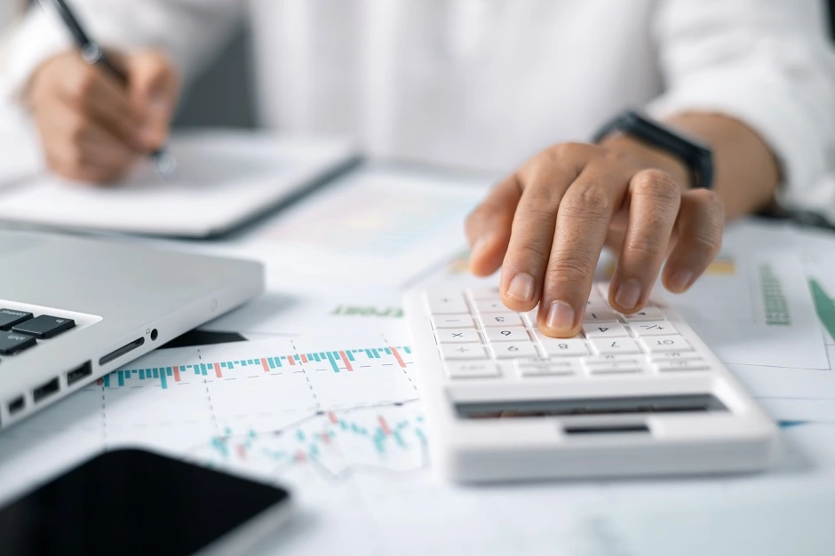 Person using a calculator beside a laptop showing financial charts