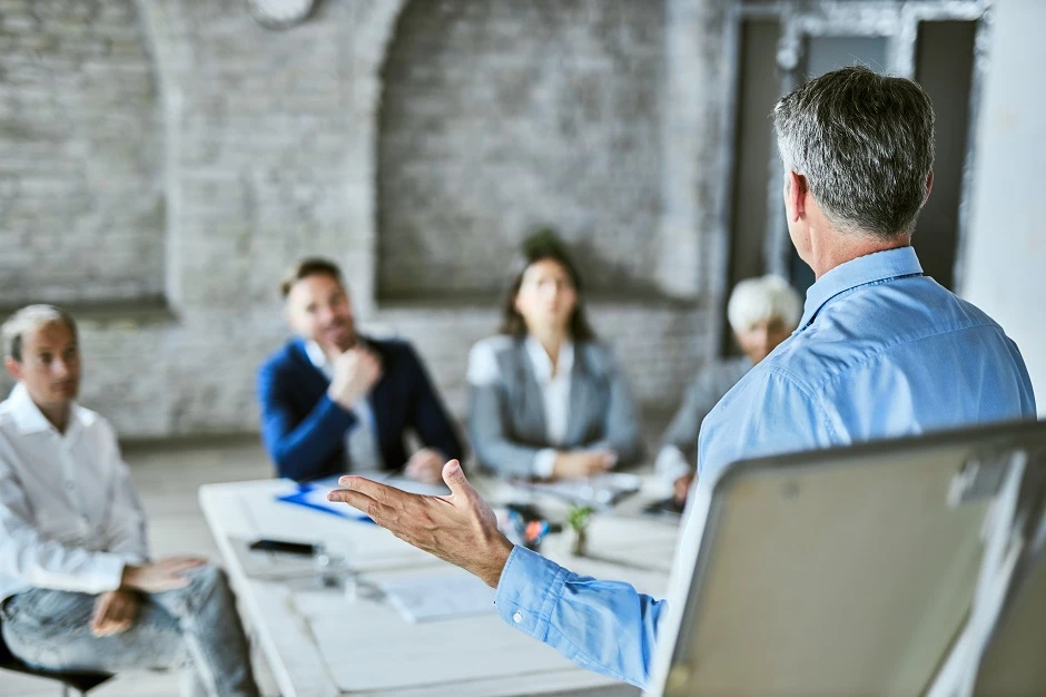 Manager in a blue shirt speaking to his team around a conference table