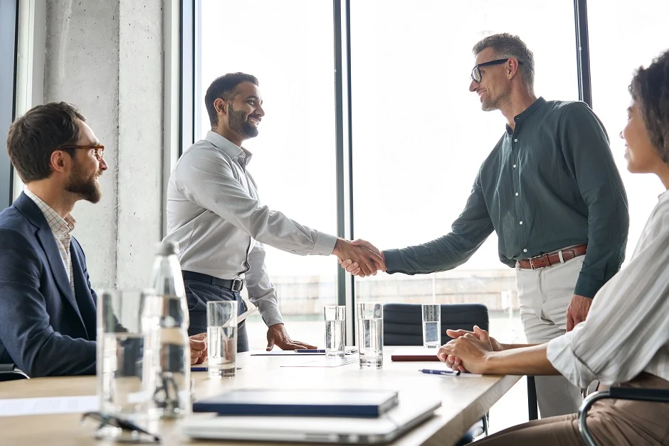 Business colleagues shaking hands across a meeting table in a bright office