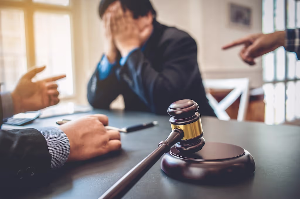 Distressed man with his face in his hands as others point at him beside a gavel