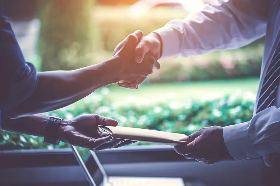 Two business people shaking hands while exchanging a document