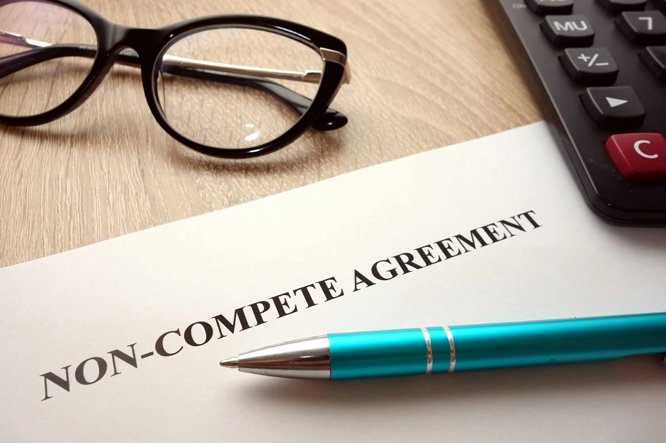 Non-compete agreement on a desk with glasses, a teal pen and a calculator