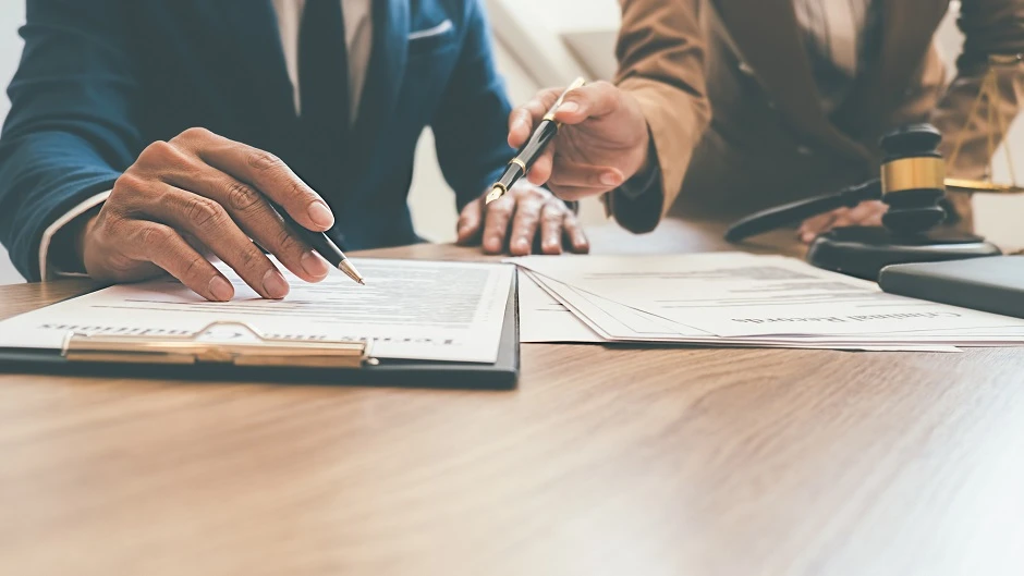 Two people reviewing and signing documents at a desk with a gavel nearby