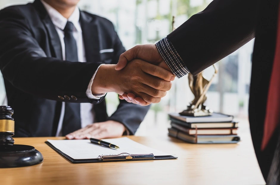 Handshake over a desk with a clipboard, gavel and Lady Justice statue