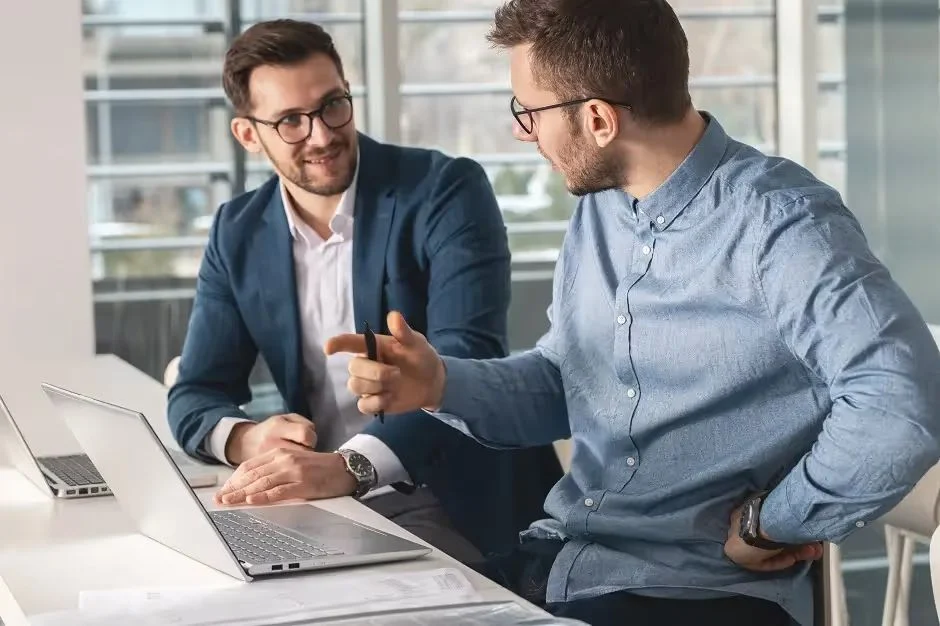 Two businessmen in glasses talking over a laptop in an office