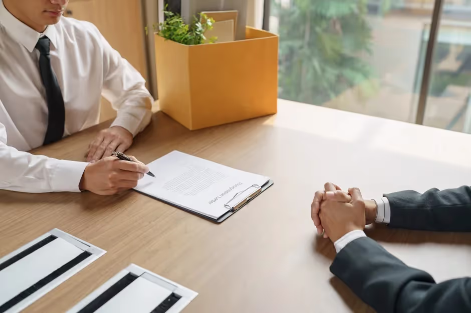 Employee with a box of belongings signing papers across from a manager