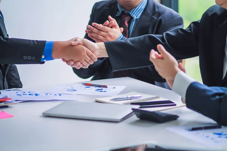 Business partners shaking hands and applauding over papers on a table