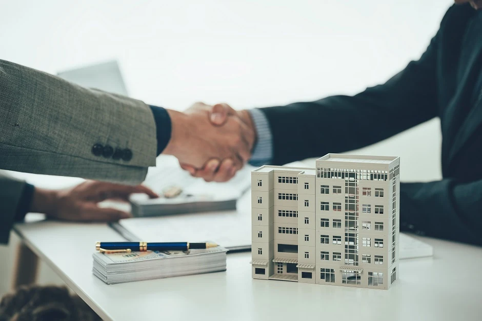 Business handshake over a table with a model apartment building and papers