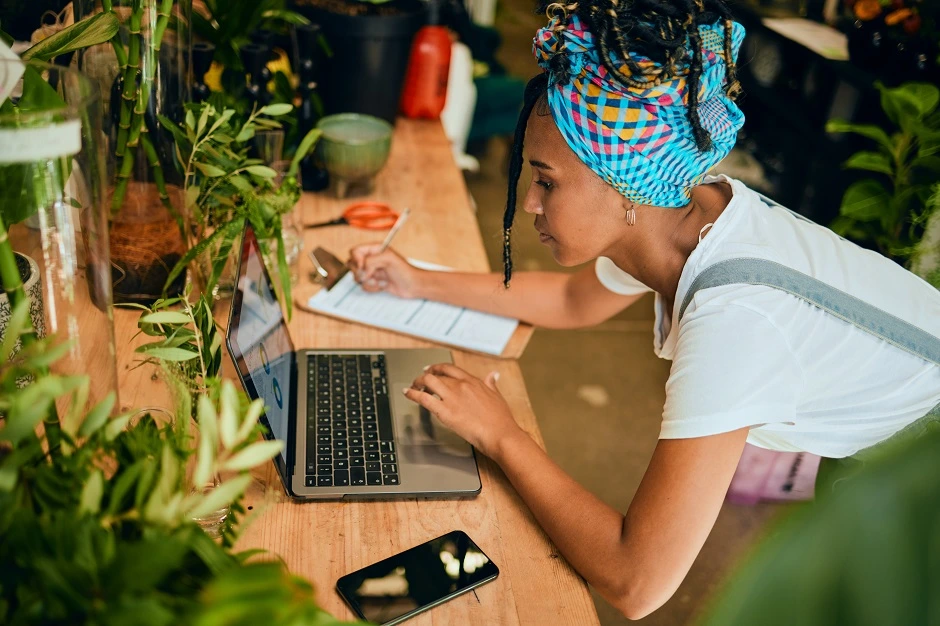 Small business owner working on a laptop at a plant-filled workbench