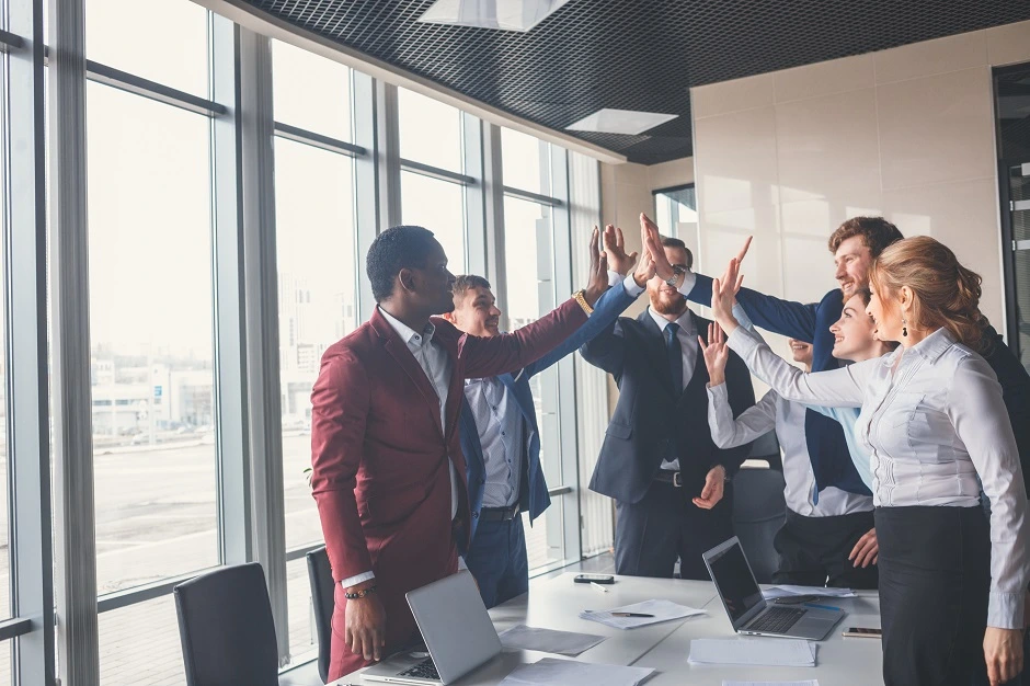 Business team giving high fives around a conference table in a bright office
