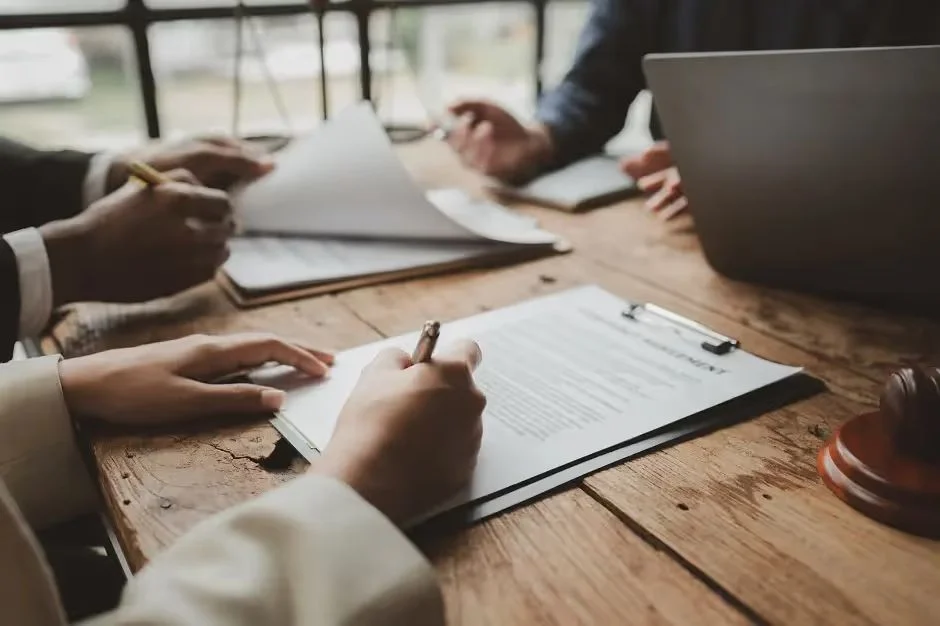 People at a wooden table reviewing and signing documents beside a gavel