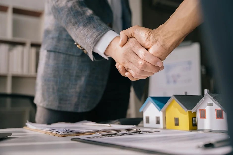 Two people shaking hands over lease documents and small model houses