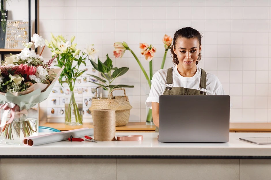 Florist smiling at her laptop at the counter of her flower shop