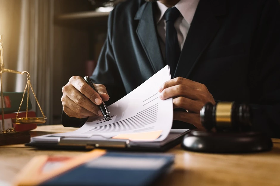 Lawyer in a suit reviewing and signing documents beside a gavel and scales